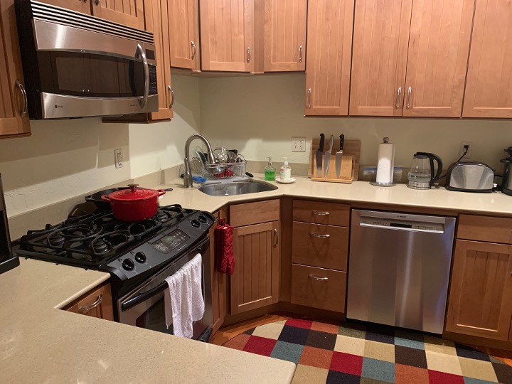 A residential kitchen with wooden cabinets, a gas stove with a red pot, sink, dishwasher, and small appliances on the counter.